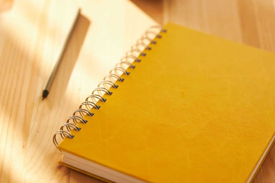 Yellow spiral notebook and a pencil on a sunlit wooden desk
