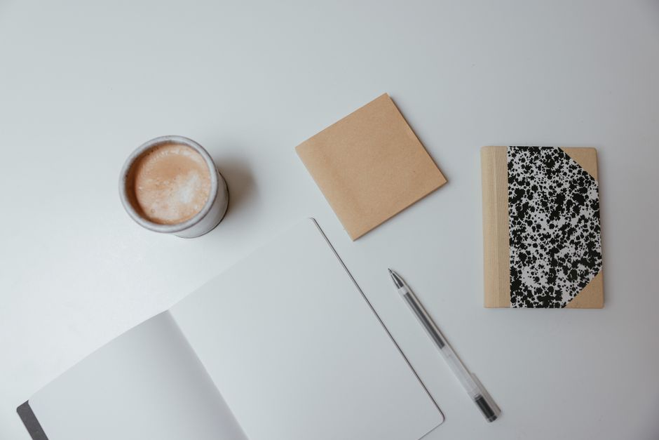 Notebooks of two different sizes and a pen laid flat next to a coffee cup