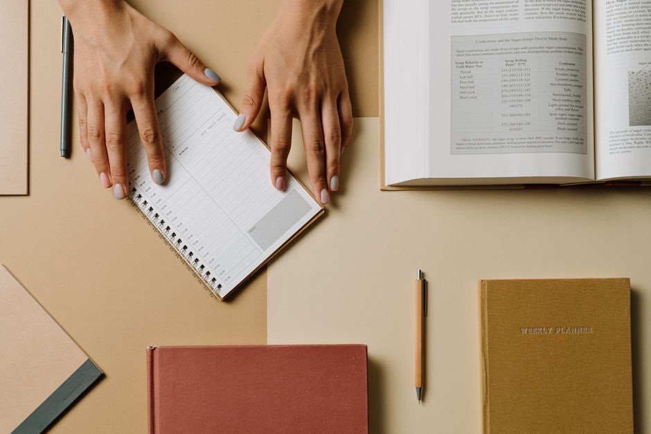 Hands arranging a paper calendar among books and notebooks on a desk